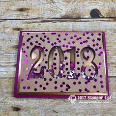 a pink and purple card with the numbers 2013 in it on a wooden surface, surrounded by confetti sprinkles