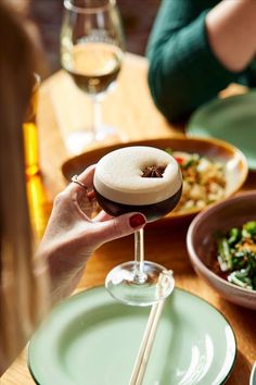 a person holding a wine glass with food on the table in front of her and two other people