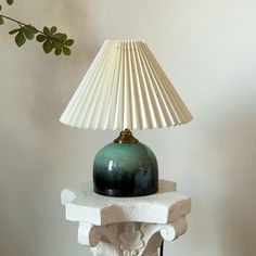 a green lamp sitting on top of a table next to a white vase and plant