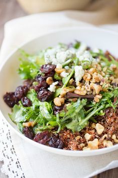 a white bowl filled with salad and nuts on top of a wooden table next to a napkin