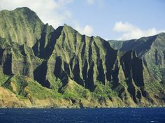 the mountains are covered in green vegetation and blue water, with a boat on the ocean below them