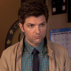 a man wearing a jacket and tie in front of a wall with calendars on it