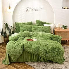 a bed with green comforter and pillows in a room next to a plant on the floor