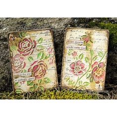 two old books with flowers on them sitting in the grass next to a rock wall