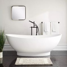 a white bath tub sitting on top of a black tiled floor next to a mirror