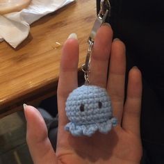 a hand holding a tiny crocheted keychain with a small blue creature on it