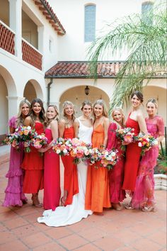 a group of women standing next to each other holding bouquets in front of a building