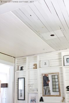 a man standing in the doorway of a white painted room with shelves and pictures on the wall