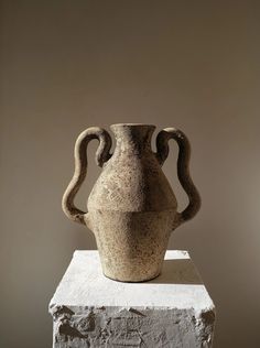 an old vase sitting on top of a block of cement in front of a wall