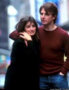 a man and woman standing next to each other on a street corner with buildings in the background