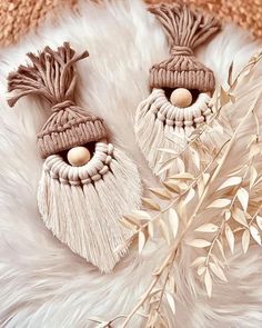 two tasseled earrings with wooden beads on top of a white fur rug next to a plant