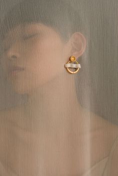 a woman's face behind a sheer curtain with a gold earring on it