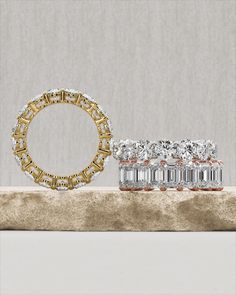 three different colored diamond rings sitting on top of a stone slab, with one ring surrounded by smaller diamonds