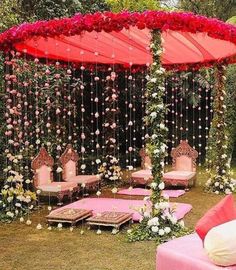 an outdoor wedding setup with pink couches and rose petals on the canopy, white flowers hanging down from the ceiling