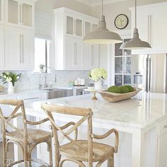 an image of a kitchen with white cabinets and marble counter tops in the middle, along with two wooden chairs