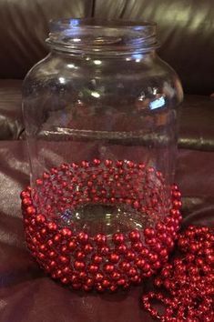 a glass jar filled with red beads sitting on top of a leather couch next to a pillow