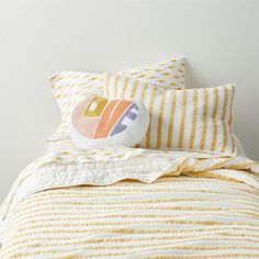 a bed with yellow and white striped comforter, pillows and pillow cases on it