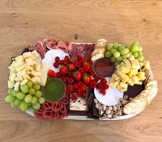 a platter filled with different types of cheeses and fruit on top of a wooden table