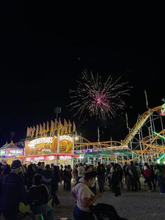 people are gathered at an amusement park with fireworks in the sky and carnival rides lit up