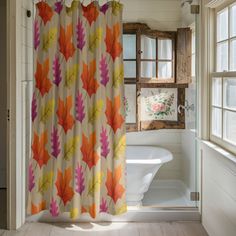 a bathroom with a bathtub, window and shower curtain that has colorful leaves on it