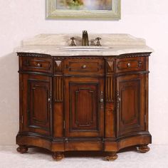 an antique bathroom vanity with marble top and wooden cabinetry, in front of a painting on the wall