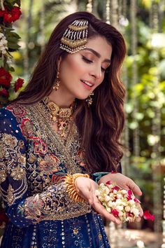 a woman in a blue dress holding flowers and wearing an elaborate head piece with gold jewelry