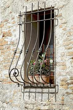 a window with iron bars and flower pots on the windowsill in an old stone building