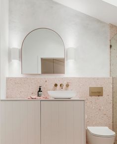 a white toilet sitting next to a sink in a bathroom under a large round mirror