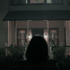 a woman standing in front of a house at night with the light on and behind her