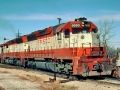 a red and white train traveling down tracks next to a dirt field on a sunny day