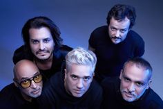 four men with white hair and glasses posing for a photo in front of a blue background