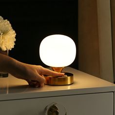 a person's hand on a table with a lamp