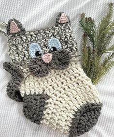 a crocheted cat ornament hanging from a tree branch on a bed