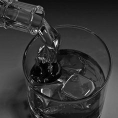 a glass filled with ice cubes and water being poured into the glass to drink