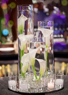 two tall clear vases with flowers in them on a table next to some glasses