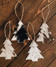 three wooden christmas trees hanging from twine on a wood table with cow hides