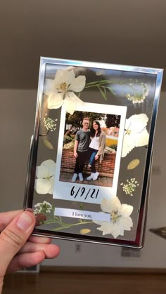 a person holding up a photo frame with white flowers on the front and bottom side