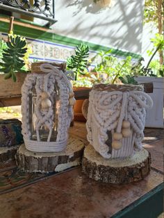 two white crocheted candle holders sitting on top of a wooden table next to potted plants