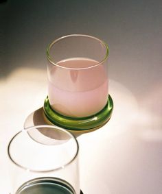 a glass filled with pink liquid sitting on top of a white table next to a green plate