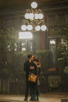 a man and woman kissing under a chandelier in an old - fashioned building