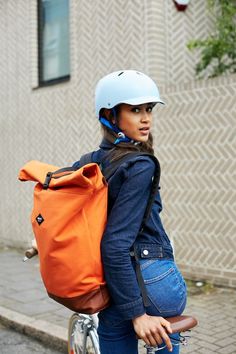 a woman riding a bike with a backpack on it's back and wearing a helmet