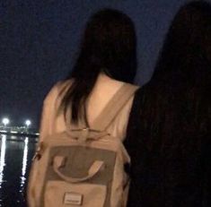 two people looking out at the water with their back to the camera and one person wearing a backpack