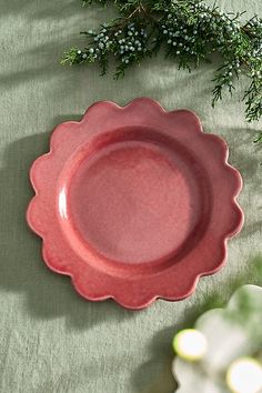 a pink plate sitting on top of a green table cloth next to a pine branch