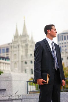 a man in a suit and tie standing on the side of a building with a book in his hand