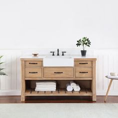 a bathroom vanity with two sinks and towels on the bottom shelf next to a potted plant