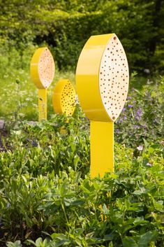 three yellow garden markers sitting in the middle of some bushes and flowers with trees in the background