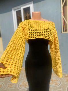 a yellow crocheted top on a mannequin with a hand holding it