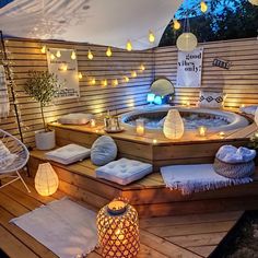 an outdoor hot tub surrounded by lights and pillows on a deck in the evening time