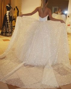 a woman in a white dress is holding up a white shawl that has glitter on it