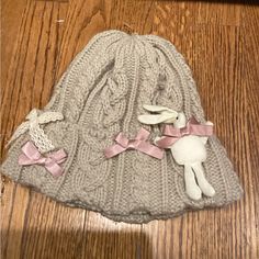 a knitted hat with pink bows and a stuffed animal on the floor next to it